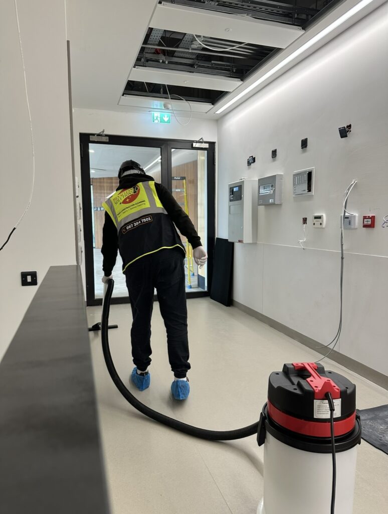 Hexaclean operative in hi-vis vest using industrial vacuum on a newly completed commercial building interior in Ireland