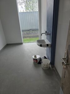 Small commercial room with wall-mounted sink and paint cans on floor before post-construction cleaning