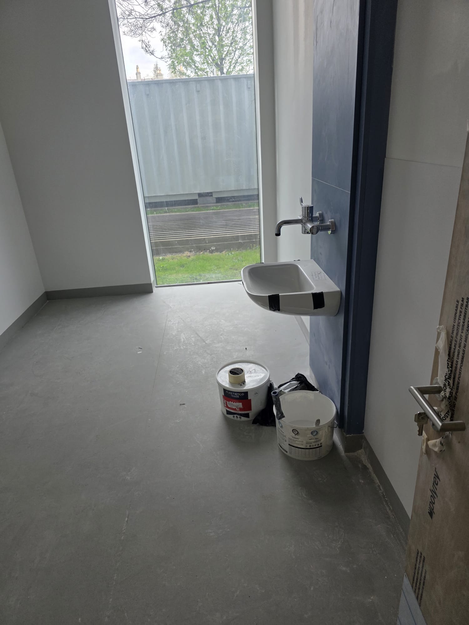 Small commercial room with wall-mounted sink and paint cans on floor before post-construction cleaning