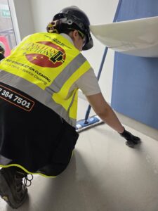 HexaClean Solutions operative in hi-vis vest and hard hat scrubbing a bathroom floor by hand during post-construction clean