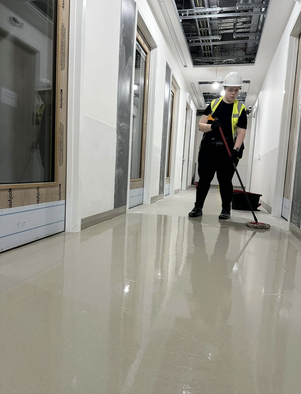 Female construction cleaning operative mopping shiny corridor floor in new-build Ireland